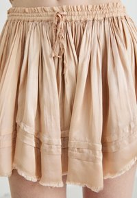 Light peach-colored skirt with gathered fabric, featuring a ruffled hem and adjustable drawstring at the waist. Soft texture and pleated design.