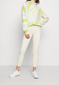 Lättvikts hooded sweatshirt med blå och grön tie-dye-mönster, ihop med slim-fit off-white byxor och vita sneakers.