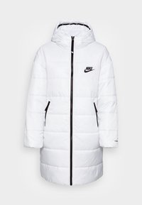 Manteau long matelassé blanc avec capuche, zip noir et poches, logo Nike sur la poitrine et petite étiquette ThermoShield sur la manche.