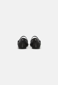 Black flat shoes featuring a textured surface, minimal design, back straps, and circular hardware detail.