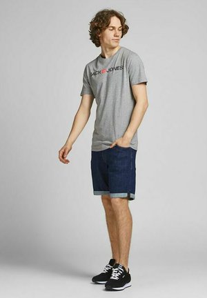 Gray short-sleeve t-shirt with "JACK & JONES" logo. Worn with denim shorts, rolled cuffs, and black sneakers with white accents.