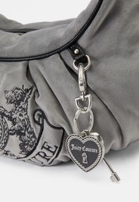 Szürke velúr táska redőzött dizájnnal, fekete bőr kiegészítőkkel és egy ezüst szív alakú lakattal, amelyen a "Juicy Couture" felirat található.