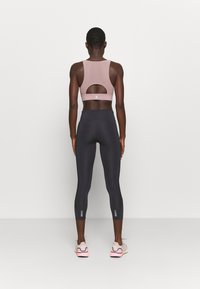 Sportbh i mjuk rosa med ett utklipp på baksidan, kombinerad med svarta leggings som har en texturerad yta och reflekterande detaljer.