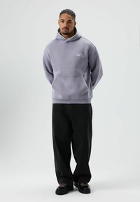 Lichtpaarse hoodie met voorzak, geribbelde manchetten en zoom. Gecombineerd met zwarte broek met wijde pijpen en zwarte veterschoenen. Soepele textuur.