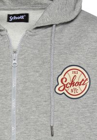 Grijze zip-up hoodie van fijn materiaal. Kenmerkt zich door een rond logo in rood en crème met "Schott NYC" en "1913." Inclusief een capuchon met trekkoorden.