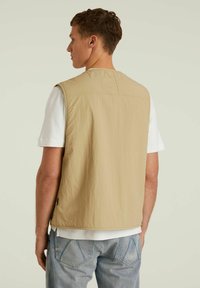 Kreemjahe seljatagune vest, mis on valmistatud kergetest kangast, iseloomustab sile tekstuur ja minimaalsed õmblustead. Seda kantakse üle valge särk ja siniste teksade.