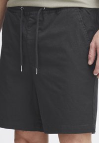 Shorts noirs en tissu léger avec une taille élastique et un cordon de serrage. Comprend deux poches latérales et une texture lisse.