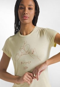 Jasnożółta koszulka z krótkim rękawem z minimalistycznym brązowym szkicem rąk oraz napisem "Re-pose" pod ilustracją.