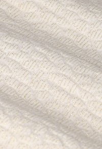 Witte stof met een getextureerd geometrisch patroon, waarin gouden vezels zijn gewoven, wat een subtiele glanseffect creëert.