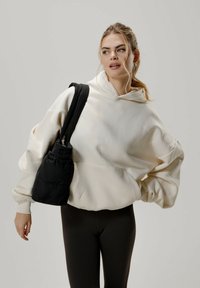 Ylihokkoinen kermahuppari, jossa on kenguru-tasku, yhdistettynä mustiin slim-fit leggareihin ja pieneen mustaan paksuun olkalaukkuun.