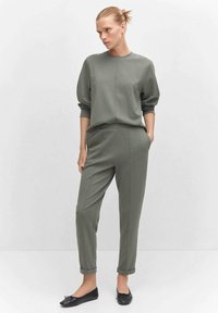 Groene bijpassende sweatshirt en tapered broek van zachte stof, met een ronde hals, omgeslagen mouwen en opgerolde enkelzoom. Zwarte platte schoenen.