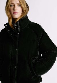 Melns samta pūdera jaka ar augstu apkakli, sprādžu pogām, raglāna piedurknēm un sānu kabatām. Mīksta tekstūra un gluda virsma.