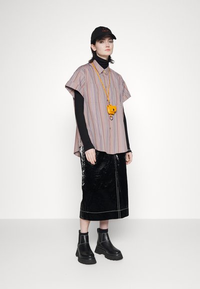 Camisa de mangas curtas às riscas em tons pastel, saia midi preta brilhante, botas pretas e uma mala de câmara amarela com um cordão correspondente.