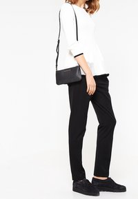 Pantaloni neri su misura abbinati a un top bianco aderente con design peplum. Una piccola borsa a tracolla nera è indossata sulla spalla.