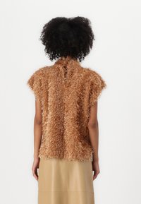 Bronse teksturert ermeløs topp med en plysjdesign, med høy krage og åpen rygg, kombinert med en beige lærskjørt.
