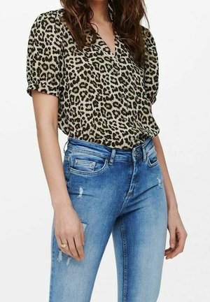 Blusa a stampa leopardata con maniche corte a sbuffo, abbinata a jeans blu a vita alta con dettagli strappati e una silhouette aderente.