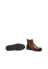 Botas de tobillo de cuero marrón con cremallera lateral, punta redonda y suela de goma texturizada que presenta un diseño de banda de rodadura con patrón.