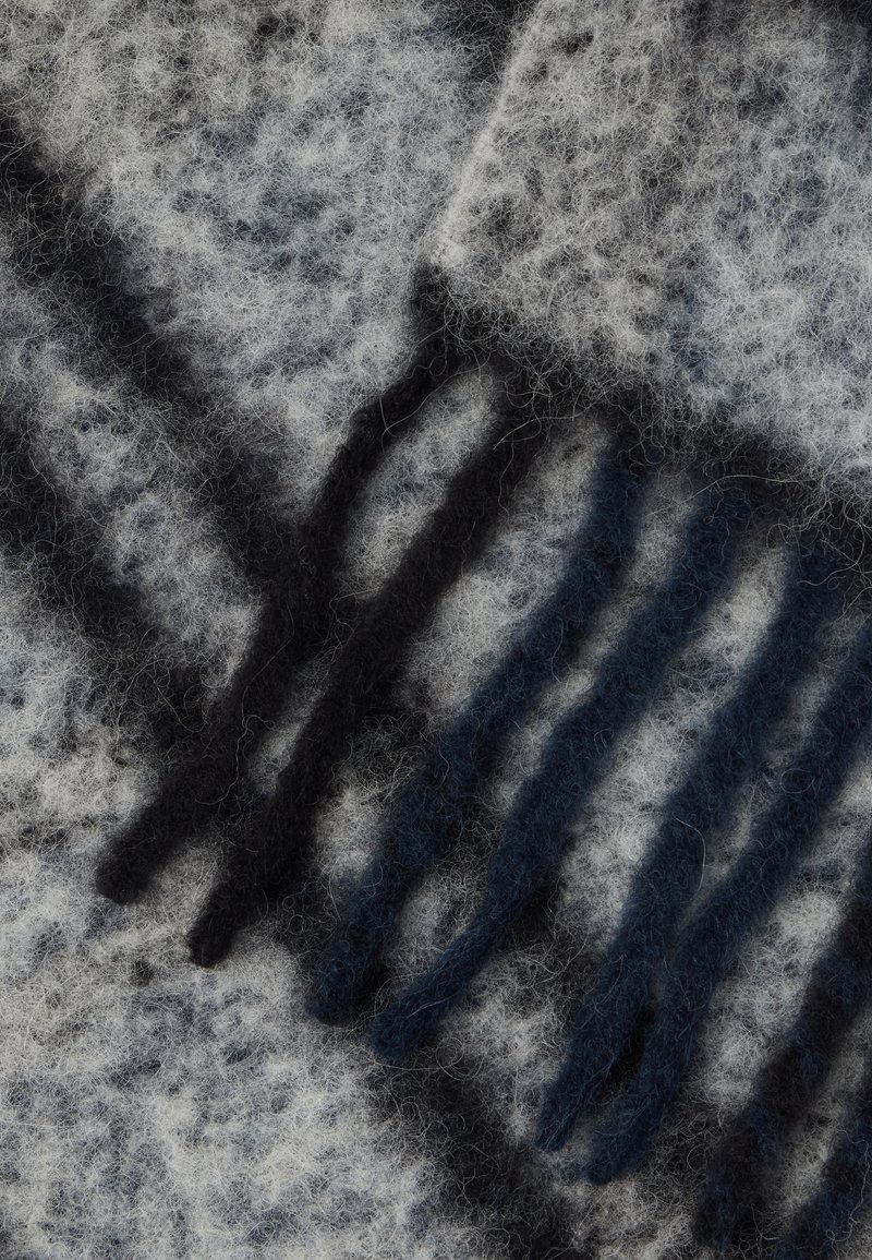 Sciarpa grigia e nera con motivo, realizzata in materiale morbido e peloso, con dettagli di frange. Presenta una combinazione di fibre chiare e scure.