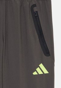 Pel�ēki sportisti bikses ar melnu kabatu ar rāvējslēdzēju un neona zaļu Adidas logo. Audums šķiet gluds, ar elastīgu jostasvietu komfortam.