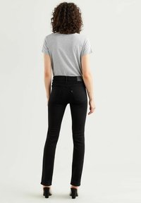 Vaqueros ajustados negros con bolsillos traseros, cintura de altura media y una textura suave, combinados con una camiseta gris ajustada. Diseño simple y clásico.