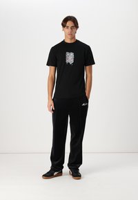Zwarte katoenen t-shirt met een grafische print van een gezicht aan de voorkant, gecombineerd met zwarte velours joggingbroek met witte accenten en logo.