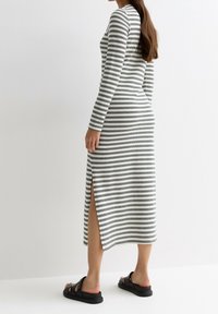 Robe longue à rayures blanches et noires, avec des fentes sur les côtés. Associée à des sandales noires, affichant une coupe décontractée.