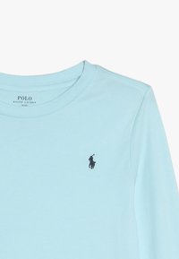 Ljusblå långärmad skjorta i bomull. Har en rundad halsringning och en liten marinblå polo-logotyp på vänster bröst. Slät textur.