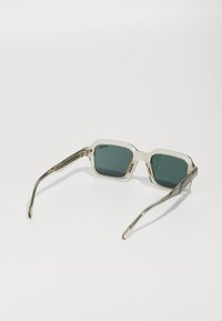 Ochelari de soare pătrați cu rame transparente, lentile gri închis și brațe din metal cu nuanță argintie, decorate cu detalii gravate.