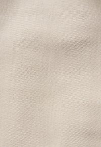 Tissu beige à texture tissée fine et surface lisse légèrement froissée.
