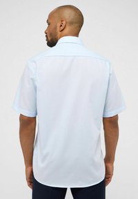 Camicetta azzurra chiara a maniche corte con colletto alla francese, texture liscia e orlo curvo, con un design posteriore senza cuciture.