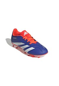 Botín de fútbol azul con acentos rojos, que presenta tres rayas blancas, una parte superior sintética texturizada y tacos rojos de goma para tracción.
