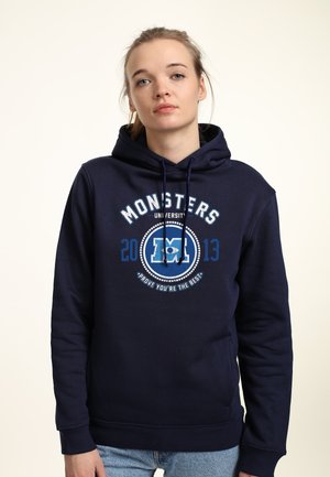 Mørkeblå hættetrøje med snore, prydet med et grafisk design, der læser "MONSTERS UNIVERSITY 2013" i hvidt og blåt, blød stofstruktur.