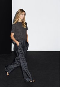 Grijze korte mouwen T-shirt gecombineerd met losse, donkere denim wijde broek met zakken. Gladde textuur en ontspannen pasvorm. Eenvoudig, minimalistisch ontwerp.