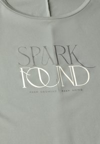 Světle zelené bavlněné tričko s kulatým výstřihem a metalickým stříbrným textem "SPARK FOUND" s podtitulem "KEEP GROWING | KEEP GOING."