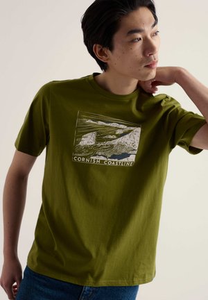 Olive green cotton T-shirt featuring a white graphic of the Cornish coastline. Crew neck design, short sleeves, and relaxed fit.