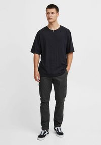 Black oversized cotton t-shirt with short sleeves, paired with dark cargo pants featuring side pockets and black and white sneakers.