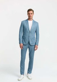 Light blue suit with a single button closure, textured fabric, and slim fit. Paired with a white t-shirt and white sneakers.