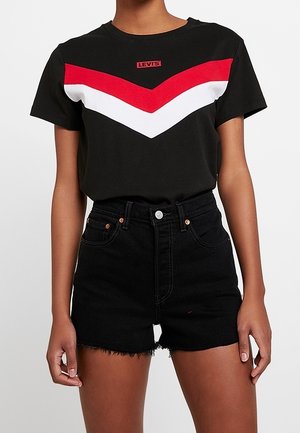 Camiseta negra con rayas en forma de chevrón rojas y blancas en el pecho, con el logo de Levi's. Un par de pantalones cortos de mezclilla negros de tiro alto con dobladillo deshilachado.