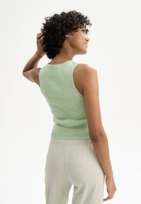 Hellgrünes, ärmelloses Strickoberteil mit tailliertem Schnitt und gerippter Textur, kombiniert mit hellbeigen, weichen Hosen mit elastischem Bund.