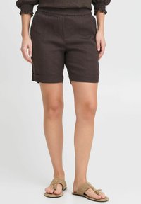 Dark brown linen shorts with an elastic waistband, rolled cuffs, and a relaxed fit. Paired with neutral sandals.