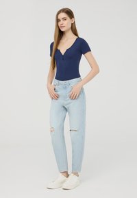 Body corto blu navy a maniche corte con scollatura a V e dettagli con bottoni, abbinato a jeans chiari a vita alta con accenti strappati. Sneakers bianche.
