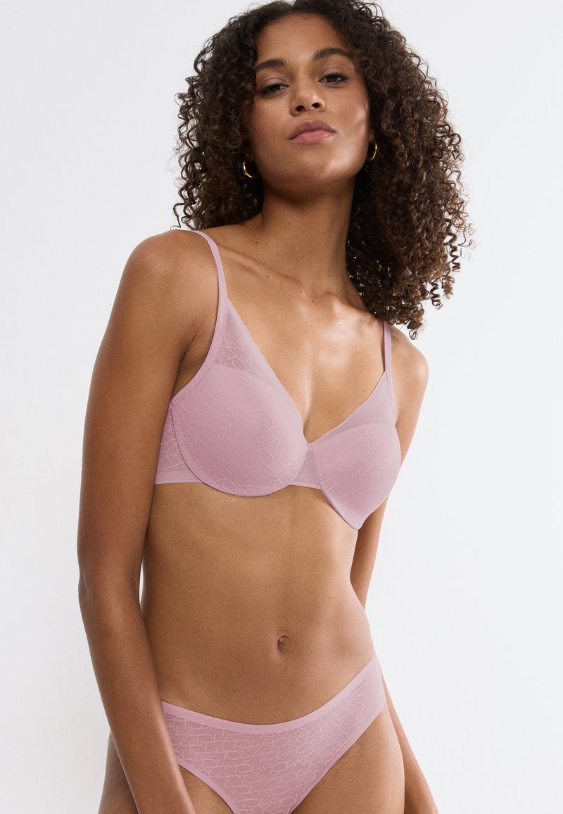 Set di lingerie rosa chiaro con un motivo a pizzo sovrapposto, spalline sottili e una texture liscia. Il reggiseno ha un design triangolare con ferretto.