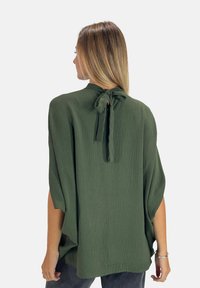 Blusa leggera verde oliva con una finitura testurizzata, dotata di un nodo nella parte posteriore del collo e maniche larghe e morbide.
