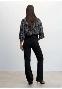 Sort denim flared jeans parret med en løs, mønstret sort og hvid bluse med bladmotiver. Struktureret stof, afslappet pasform.