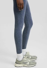 Högmidjade, marinblå tights med mjuk textur och sidoseamsdetaljer, i kombination med grå sportskor och vita strumpor.