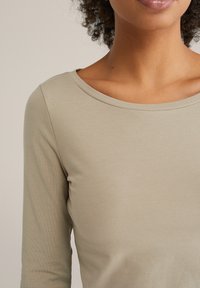 Šviesiai smėlio spalvos ilgomis rankovėmis viršus iš lygaus audinio, su apvalia iškirpte, subtilia siūle ir prigludusia forma.