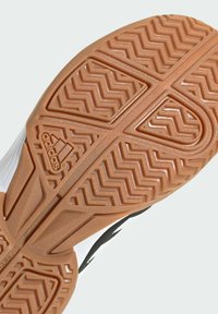 Semelle en caoutchouc avec un motif de traction en zigzag, associée à une tige synthétique blanche et noire, arborant le logo "adidas".