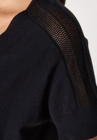 Maglione nero con una morbida texture a maglia e dettagli in mesh sulle spalle e maniche corte, che offre un effetto di design a strati.