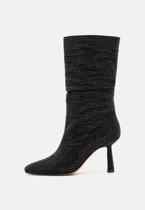 Botín negro de tobillo con textura arrugada, puntera puntiaguda y tacón delgado. La superficie presenta un patrón de cuadrícula con pequeños detalles en relieve.