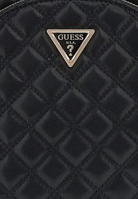 Borsa a tracolla nera trapuntata con una placca logo dorata a forma triangolare con il testo "GUESS U.S.A." su una superficie in pelle testurizzata.
